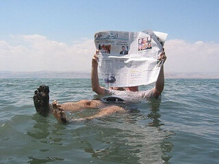 Hombre flotando leyendo el periódico en el Mar Muerto